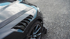 Black BMW G82 M4 track build with carbon fiber vented fenders, side skirts, rear diffuser, and oversized GT wing parked at a professional racing circuit pit lane.