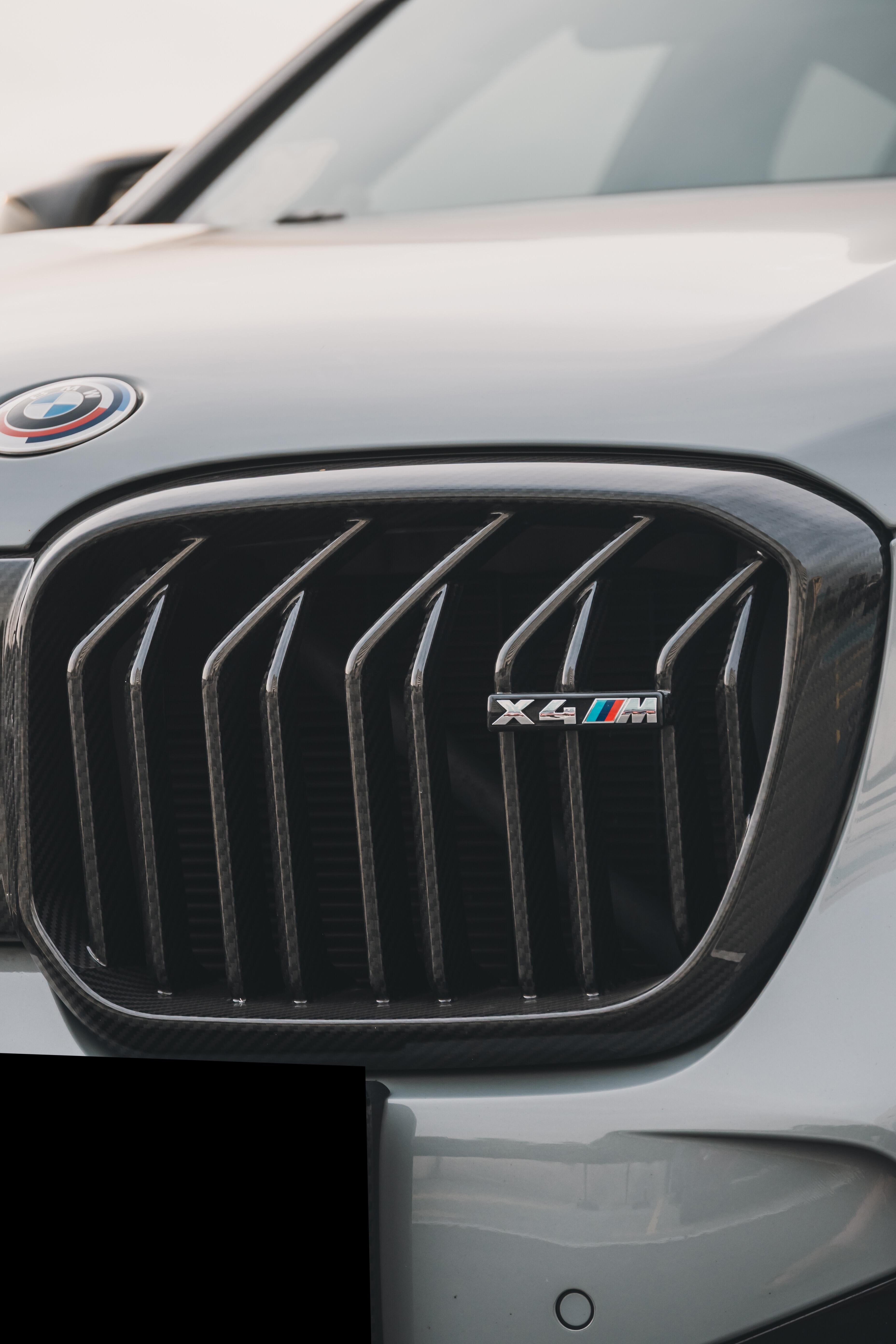 White BMW X4M featuring a REVOZPORT front grille upgrade and sporty front-end styling parked on an open urban road.