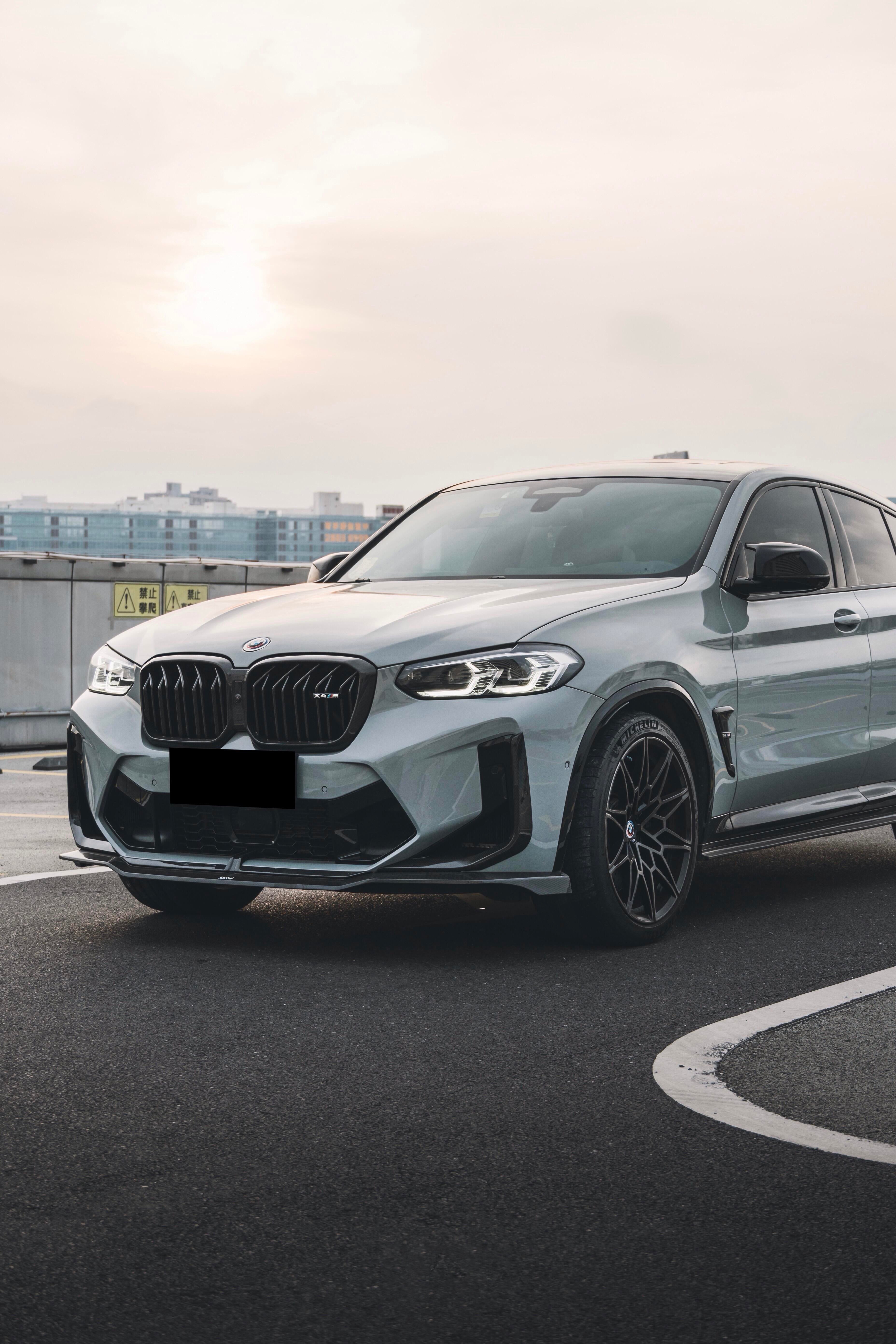White BMW X4M featuring a REVOZPORT front grille upgrade and sporty front-end styling parked on an open urban road.