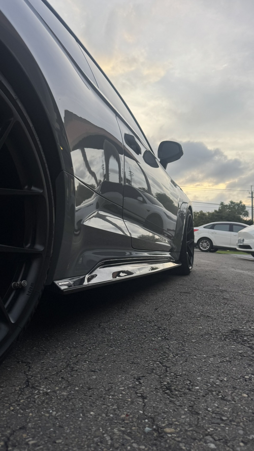 Gray Audi RS5 Sportback featuring a REVOZPORT carbon fiber front lip, side skirts, and aggressive front aero styling parked outdoors near tropical landscaping.