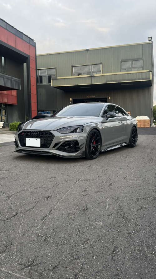 Gray Audi RS5 Sportback featuring a REVOZPORT carbon fiber front lip, side skirts, and aggressive front aero styling parked outdoors near tropical landscaping.