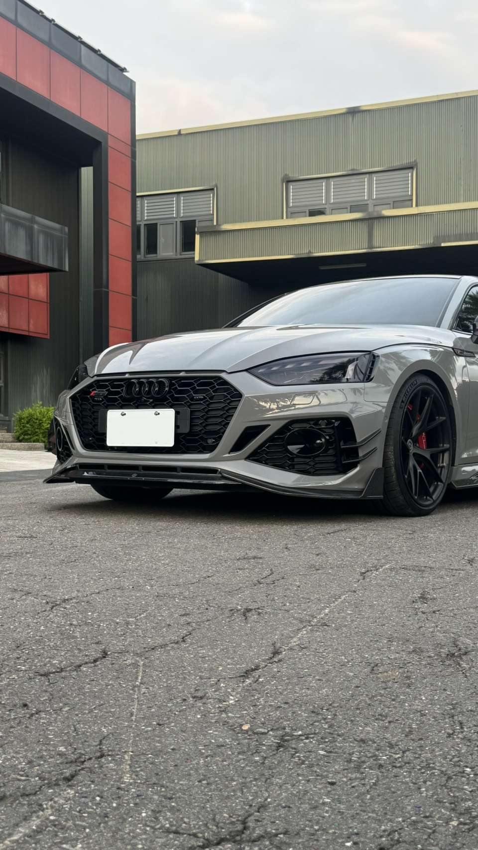 Gray Audi RS5 Sportback featuring a REVOZPORT carbon fiber front lip, side skirts, and aggressive front aero styling parked outdoors near tropical landscaping.