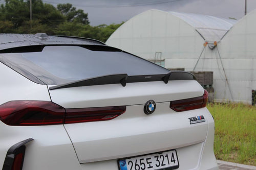 Front view of a white BMW X6M featuring an aggressive REVOZPORT front bumper and carbon fiber aero styling parked on a quiet urban street.