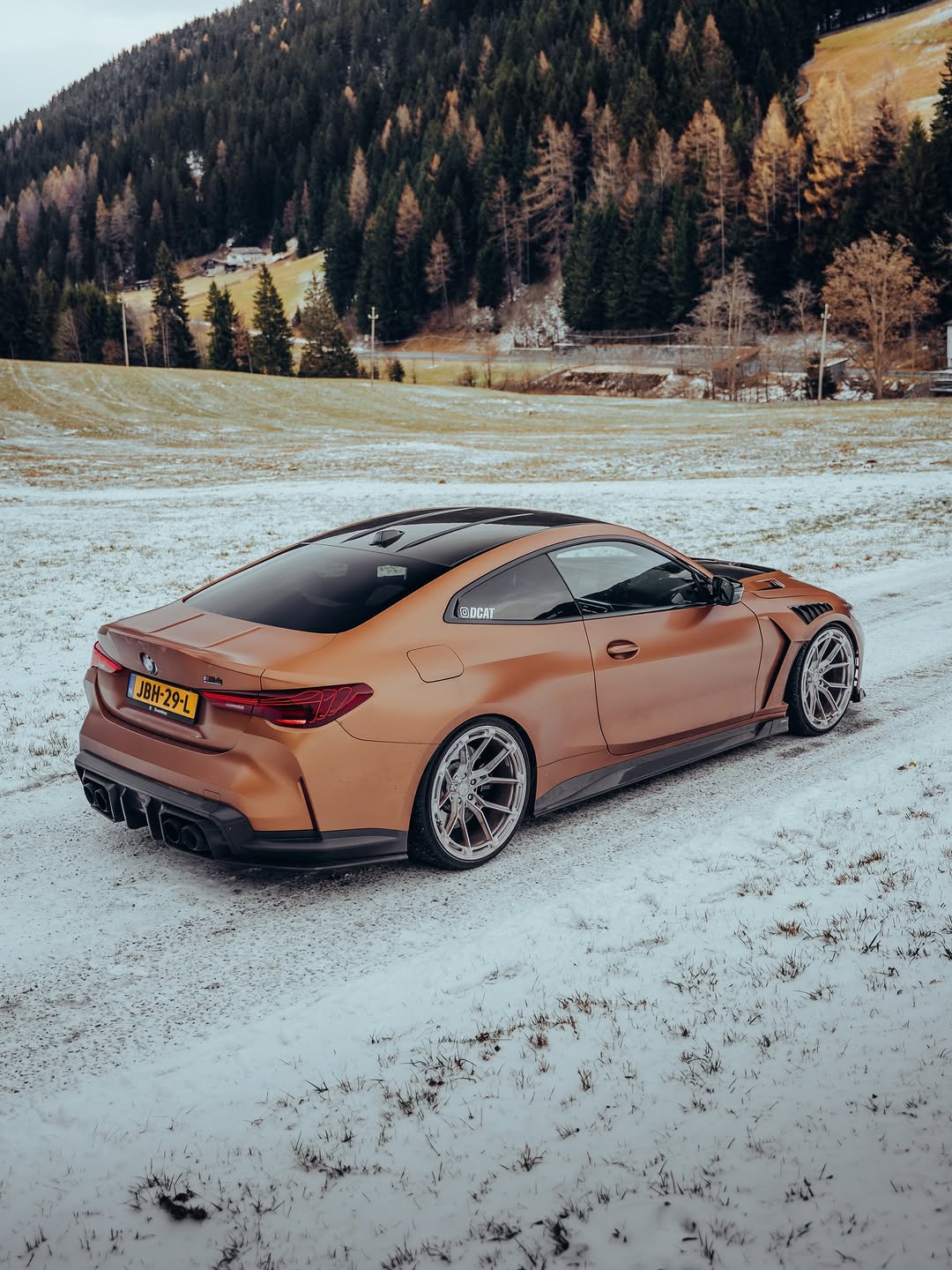 Close-up of REVOZPORT forged multi-spoke wheels mounted on a bronze widebody sports car with carbon fiber aero details on a snowy road.
