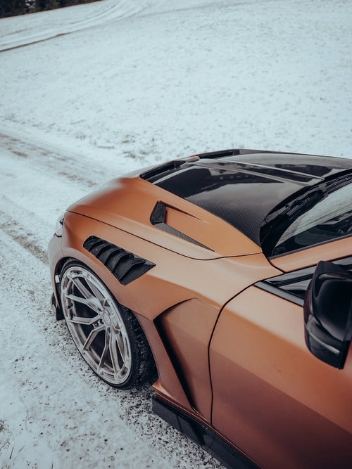 Close-up of REVOZPORT forged multi-spoke wheels mounted on a bronze widebody sports car with carbon fiber aero details on a snowy road.