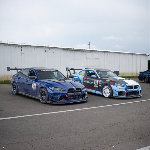 Close-up of a blue wide-body performance car featuring aggressive aerodynamic fender vents, extended side skirts, and lightweight multi-spoke wheels. The image highlights the custom bodywork, low-profile performance tire, and carbon fiber aero details in an outdoor automotive setting.