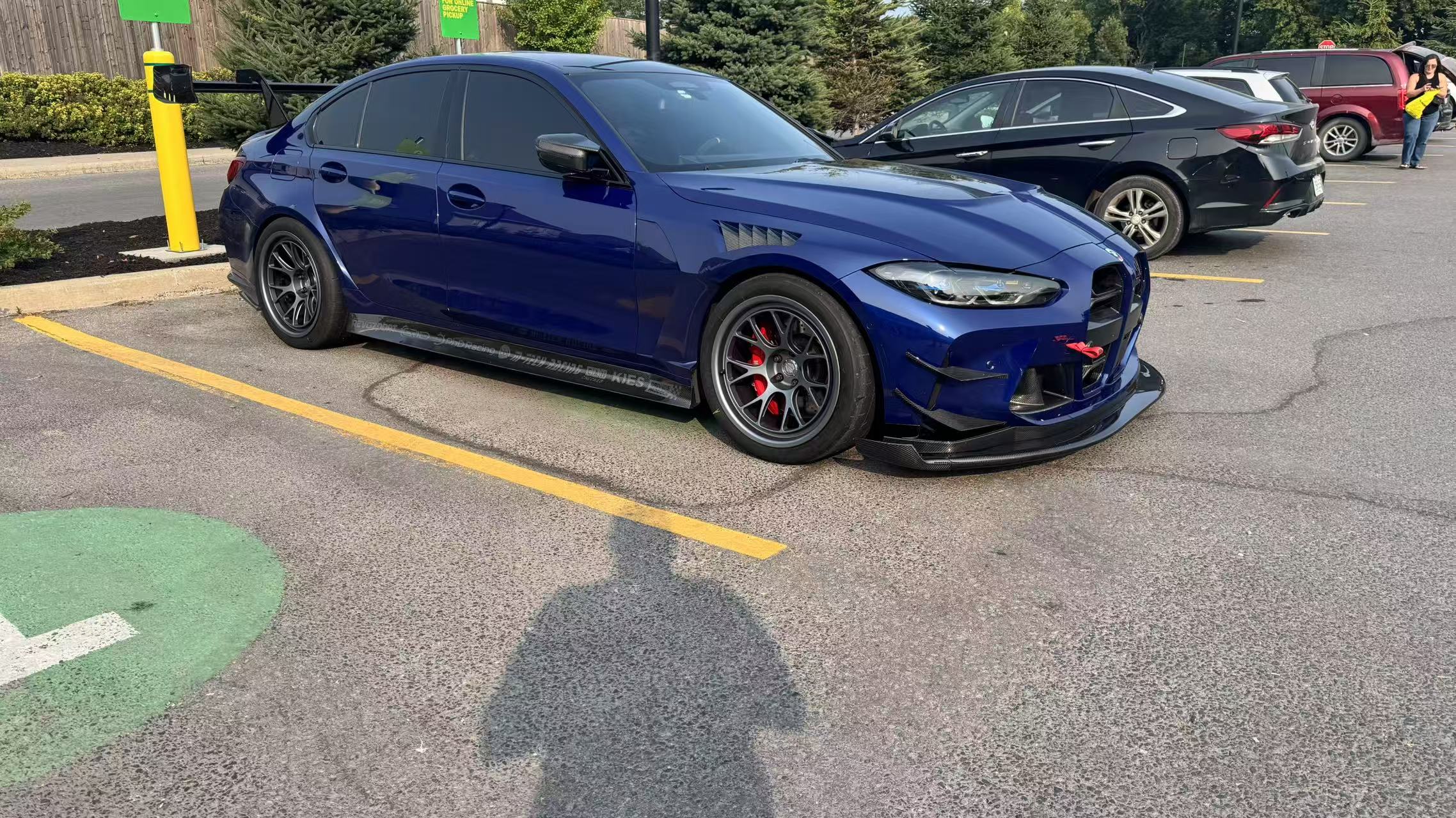 Close-up of a blue wide-body performance car featuring aggressive aerodynamic fender vents, extended side skirts, and lightweight multi-spoke wheels. The image highlights the custom bodywork, low-profile performance tire, and carbon fiber aero details in an outdoor automotive setting.