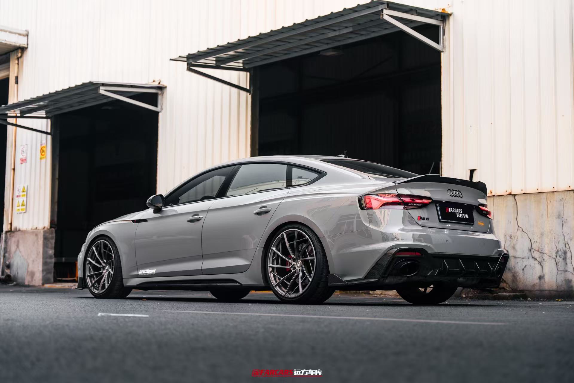 Gray Audi RS5 Sportback fitted with REVOZPORT forged multi-spoke wheels, parked outside an industrial garage.