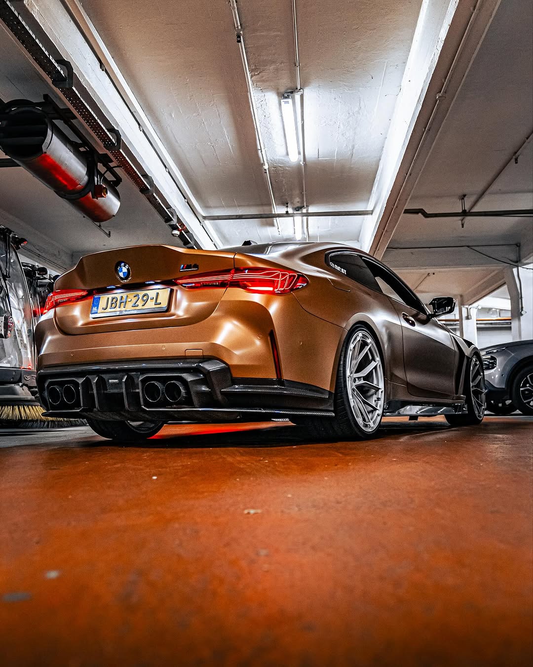 Bronze BMW G82 M4 fitted with REVOZPORT forged silver multi-spoke wheels, parked on a luxury city street alongside a matching Audi RS model.