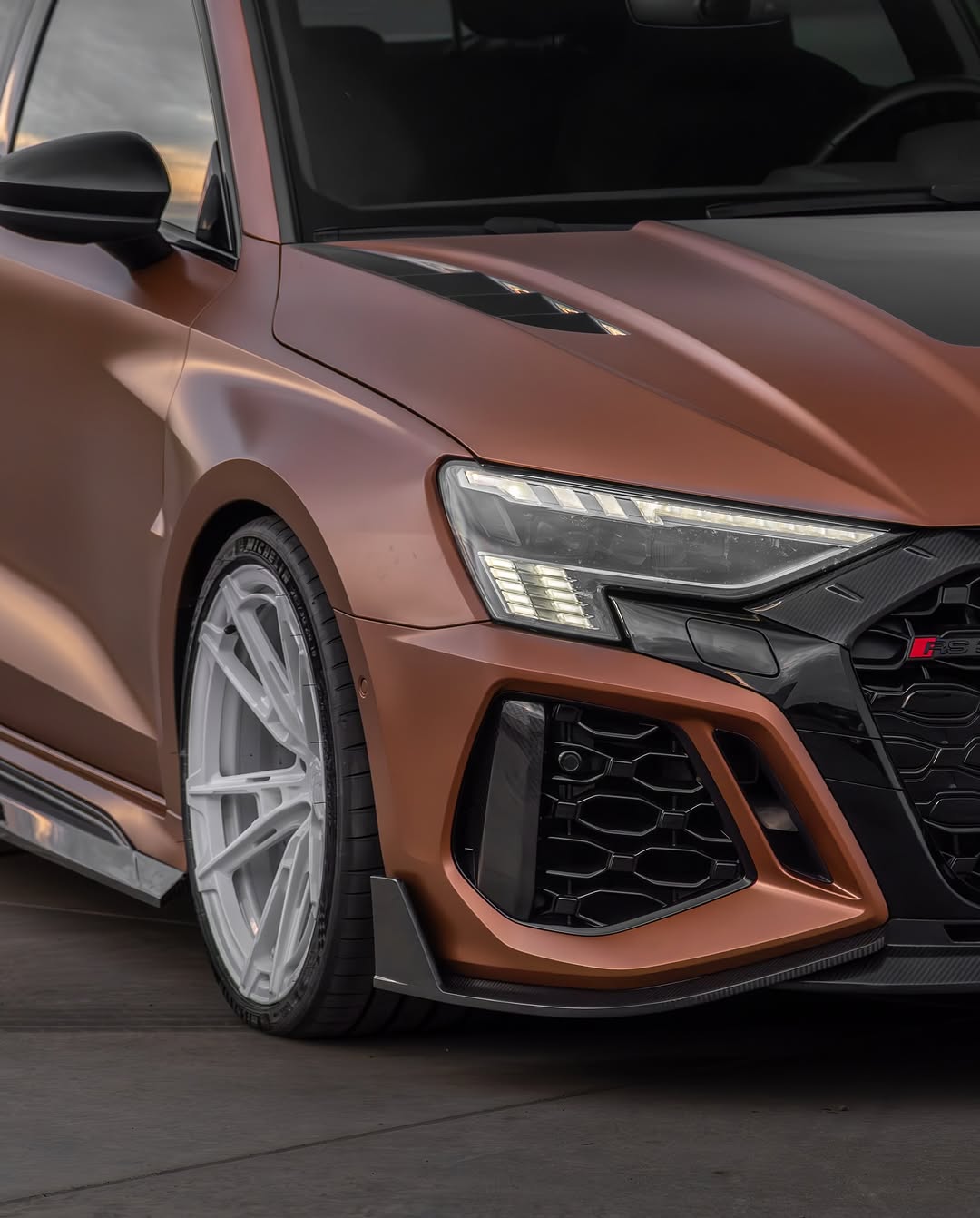 Bronze Audi RSQ8 featuring an aggressive REVOZPORT carbon fiber body kit with front lip, hood vents, side skirts, and custom front bumper design at sunset.