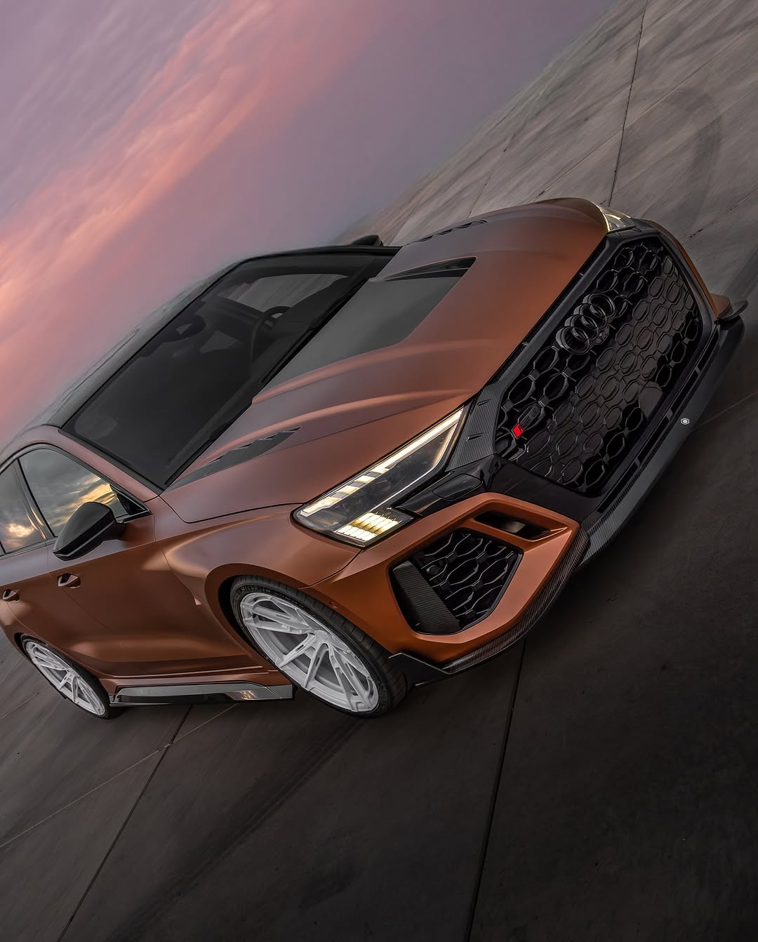 Bronze Audi RSQ8 featuring an aggressive REVOZPORT carbon fiber body kit with front lip, hood vents, side skirts, and custom front bumper design at sunset.