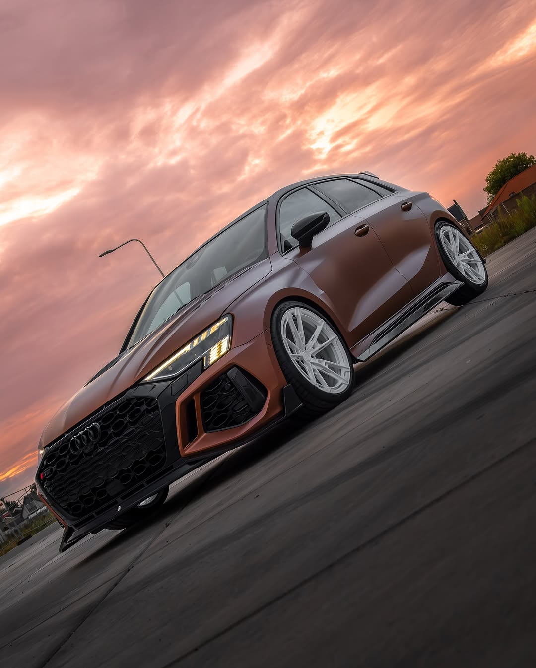 Bronze Audi RSQ8 featuring an aggressive REVOZPORT carbon fiber body kit with front lip, hood vents, side skirts, and custom front bumper design at sunset.