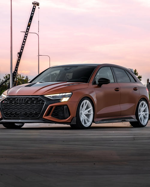 Bronze Audi RSQ8 featuring an aggressive REVOZPORT carbon fiber body kit with front lip, hood vents, side skirts, and custom front bumper design at sunset.