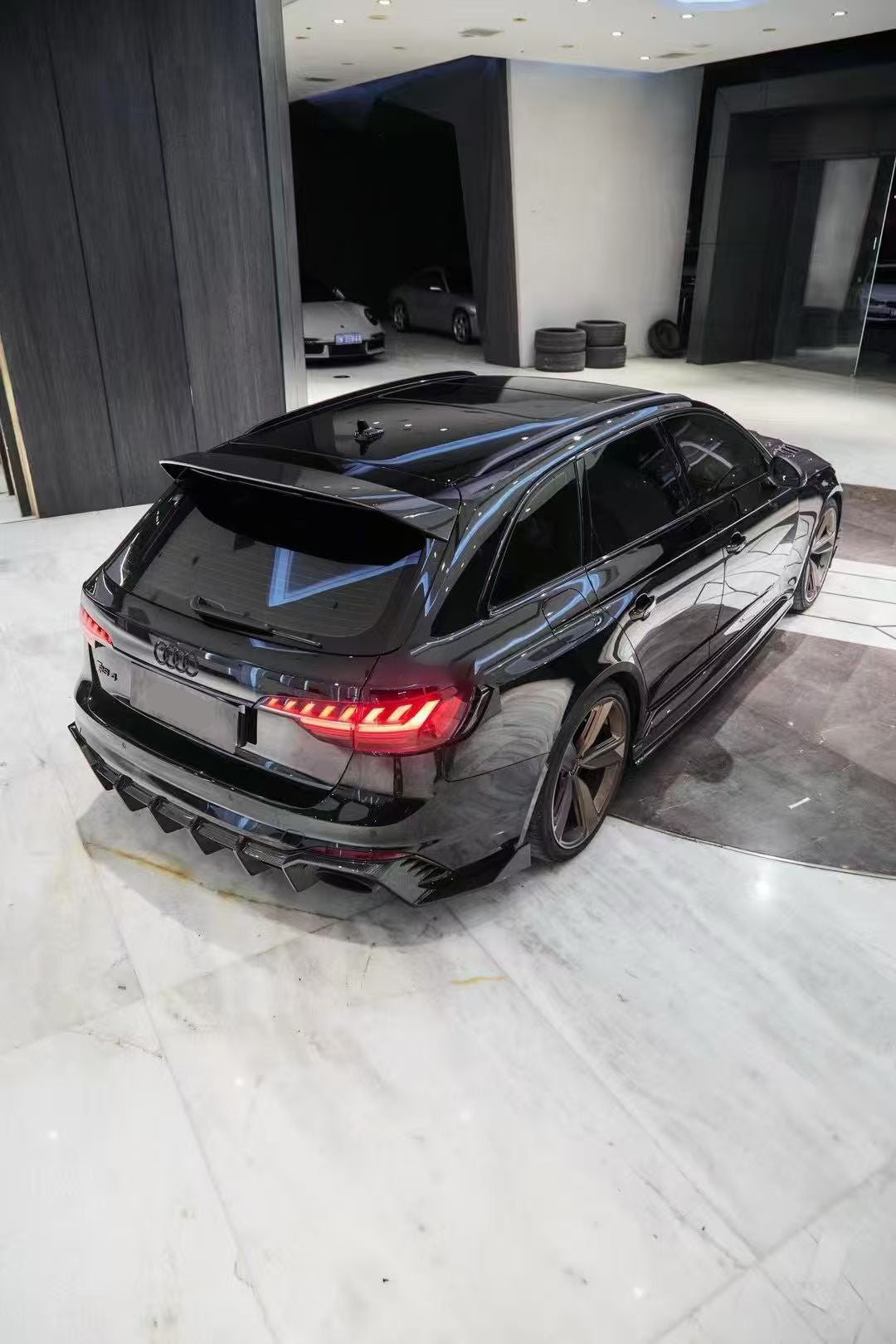 Black Audi RS4 Avant featuring a REVOZPORT carbon fiber body kit with front lip, side skirts, and aggressive aero styling displayed inside a luxury showroom.