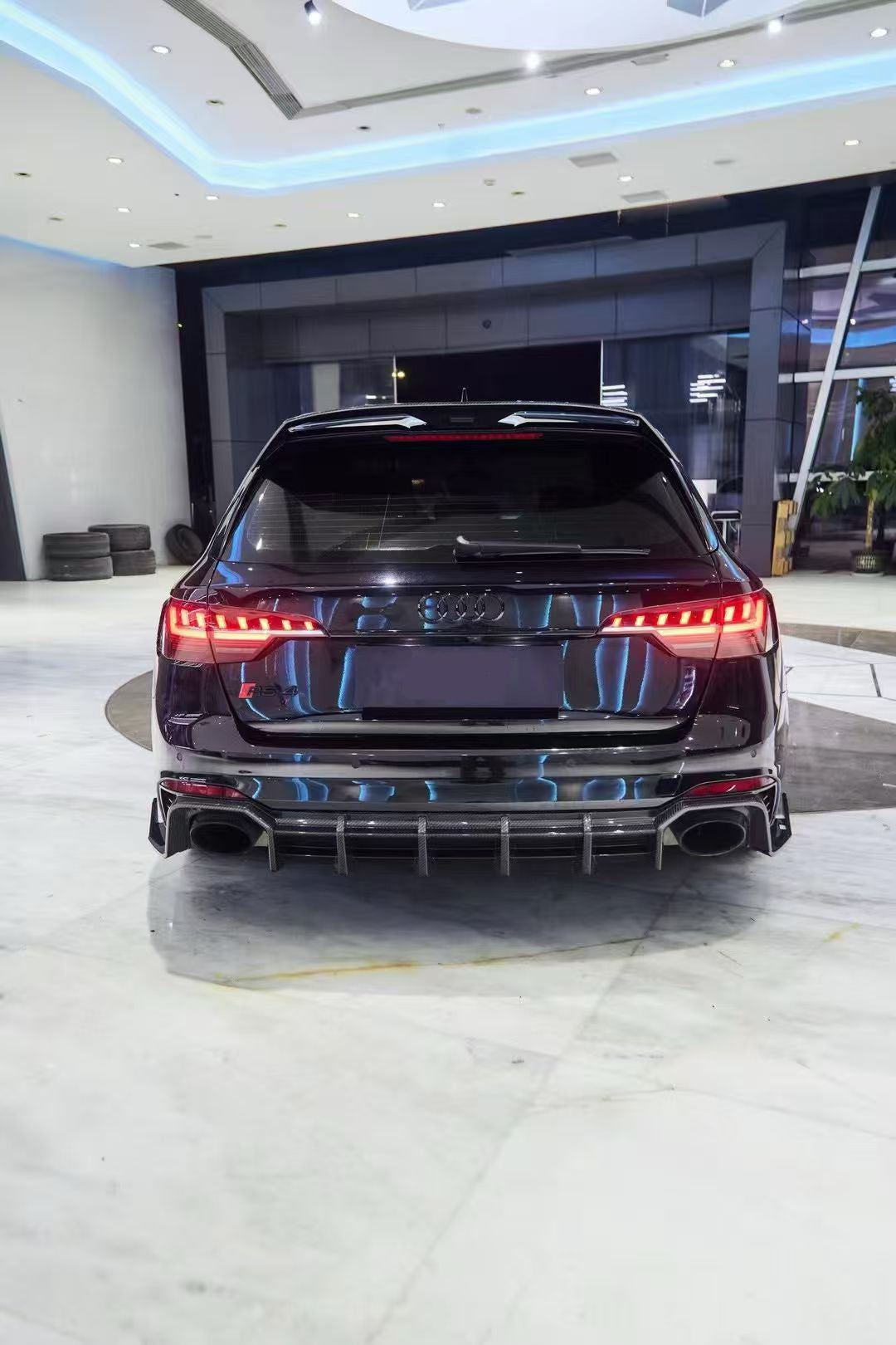 Black Audi RS4 Avant featuring a REVOZPORT carbon fiber body kit with front lip, side skirts, and aggressive aero styling displayed inside a luxury showroom.