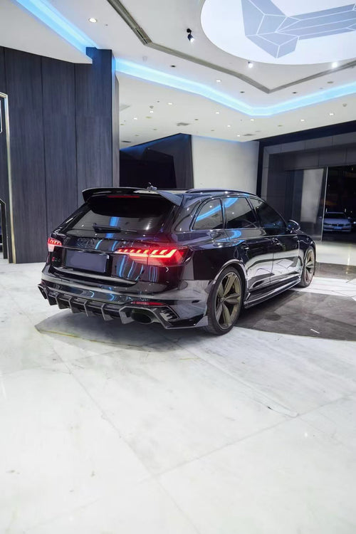 Black Audi RS4 Avant featuring a REVOZPORT carbon fiber body kit with front lip, side skirts, and aggressive aero styling displayed inside a luxury showroom.