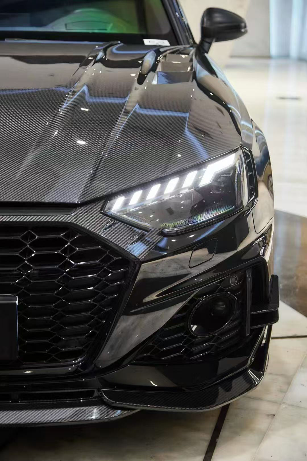 Black Audi RS4 Avant featuring a REVOZPORT carbon fiber body kit with front lip, side skirts, and aggressive aero styling displayed inside a luxury showroom.