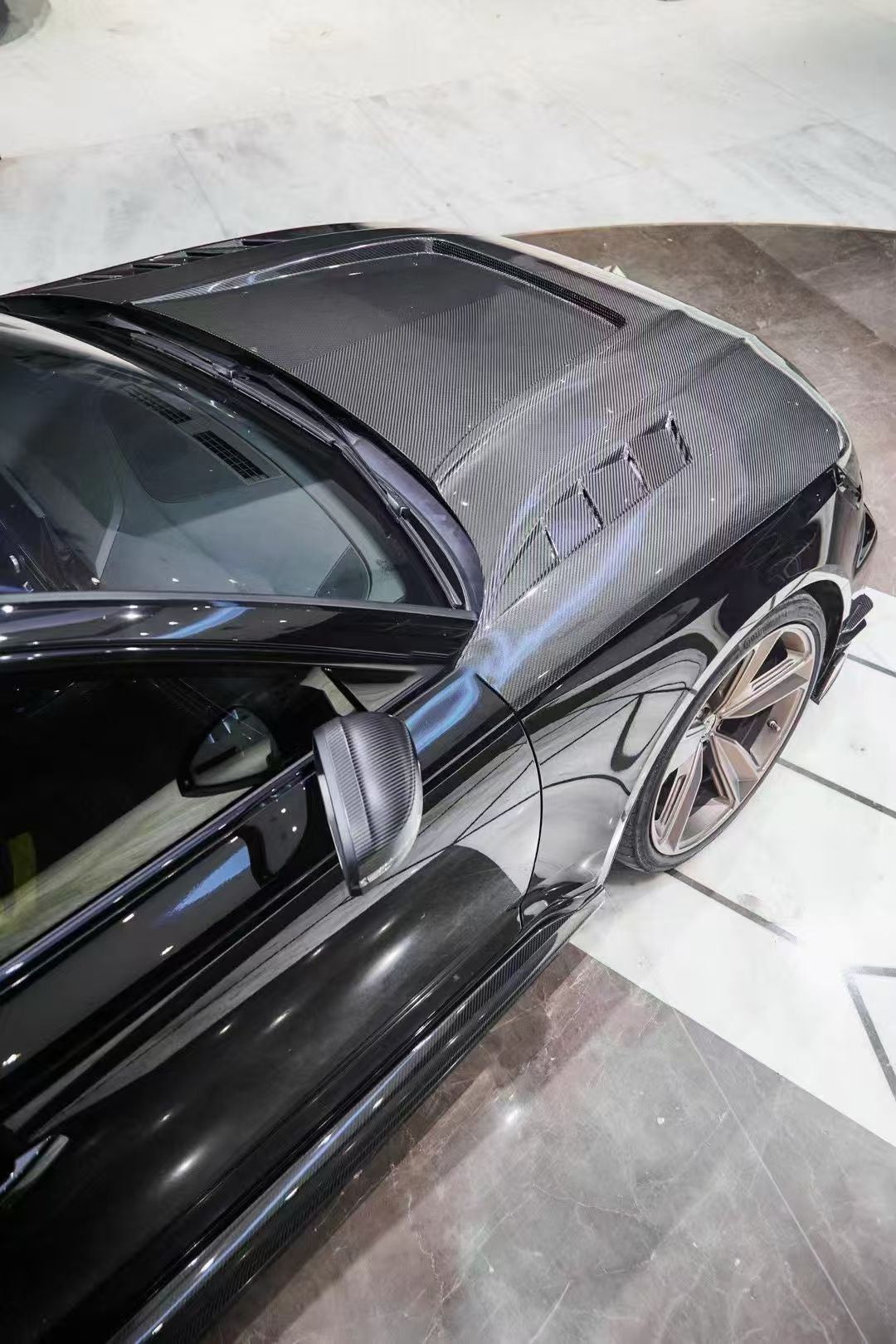 Black Audi RS4 Avant featuring a REVOZPORT carbon fiber body kit with front lip, side skirts, and aggressive aero styling displayed inside a luxury showroom.