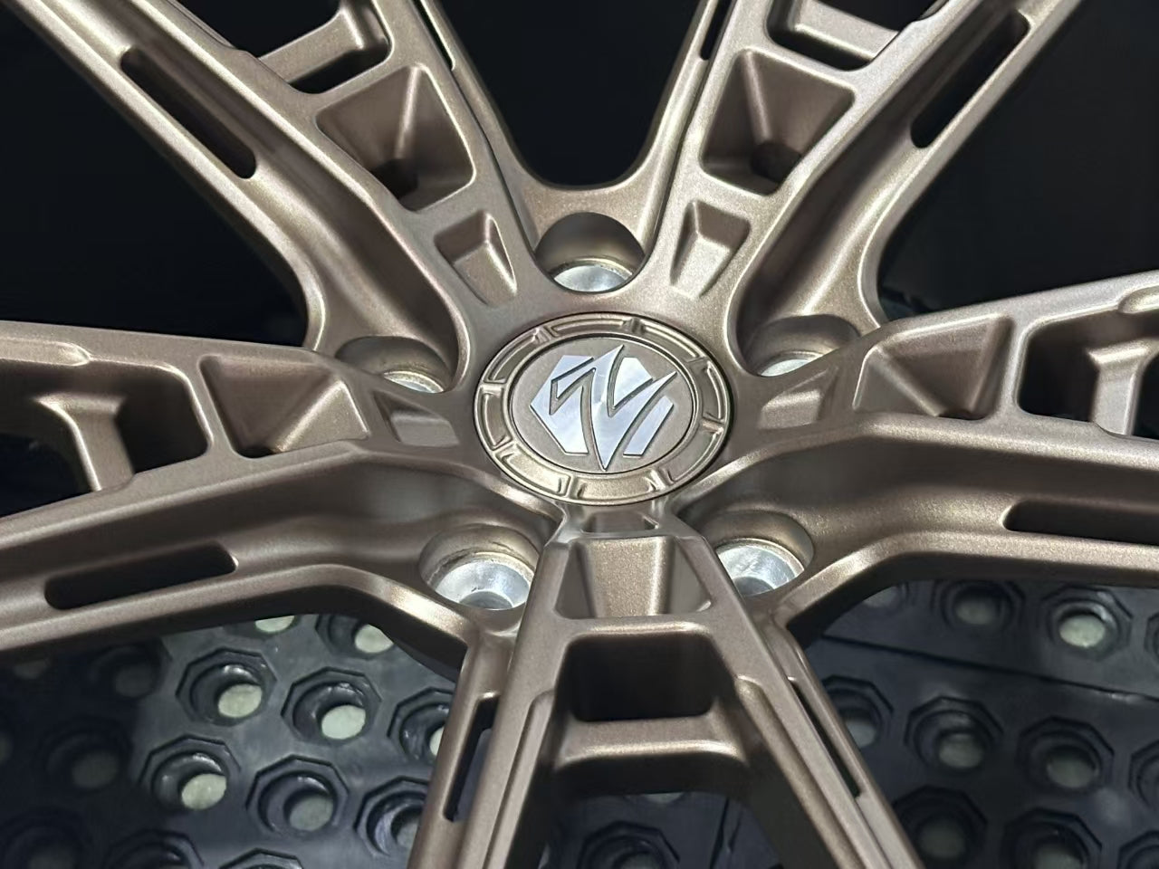 Bronze REVOZPORT forged alloy wheel with an intricate split multi-spoke design displayed on a black textured workshop floor.