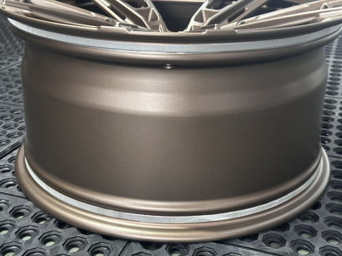 Bronze REVOZPORT forged alloy wheel with an intricate split multi-spoke design displayed on a black textured workshop floor.