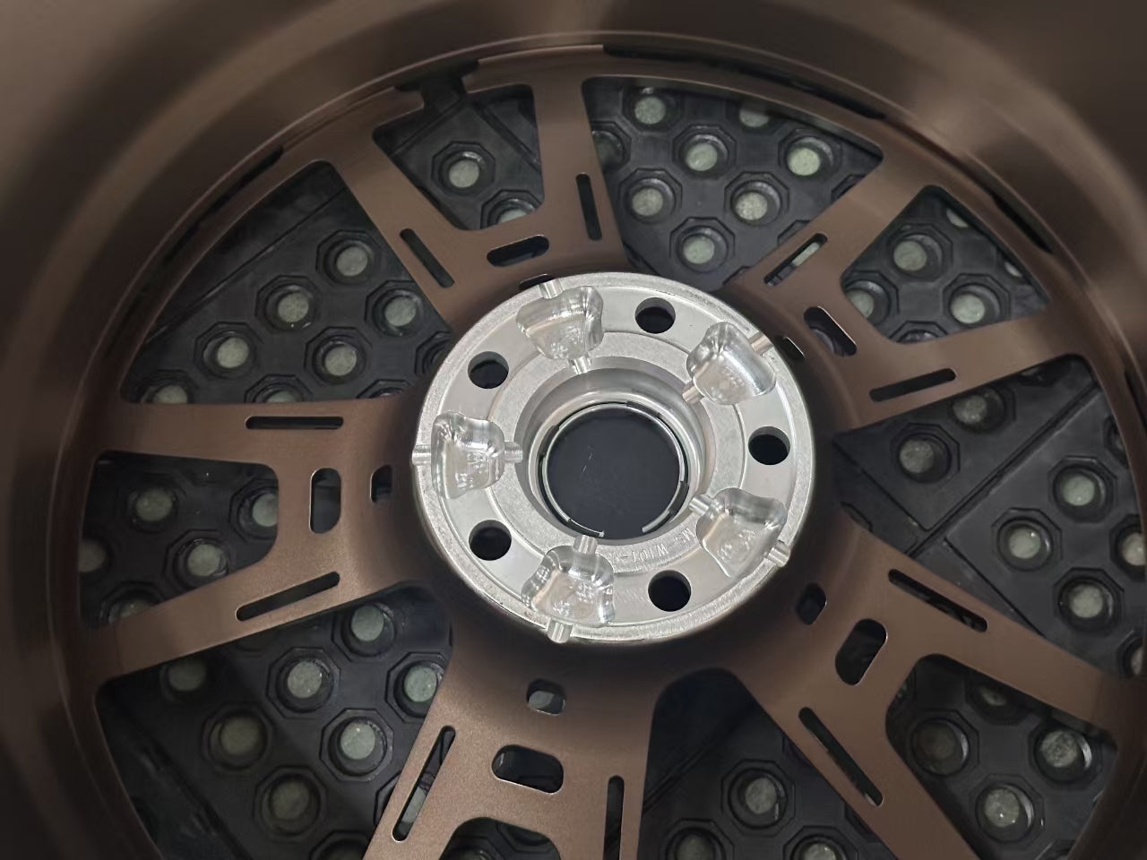 Bronze REVOZPORT forged alloy wheel with an intricate split multi-spoke design displayed on a black textured workshop floor.