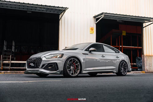Gray Audi RS5 Sportback fitted with REVOZPORT forged multi-spoke wheels, parked outside an industrial garage.