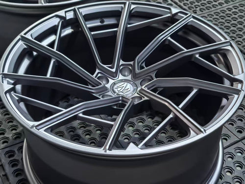 Matte gray REVOZPORT forged alloy wheel with an intricate split multi-spoke design displayed on a black textured workshop floor.