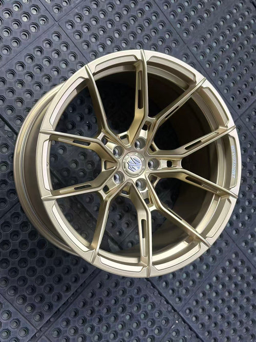 Bronze REVOZPORT forged alloy wheel with split multi-spoke design displayed on a black textured workshop floor.