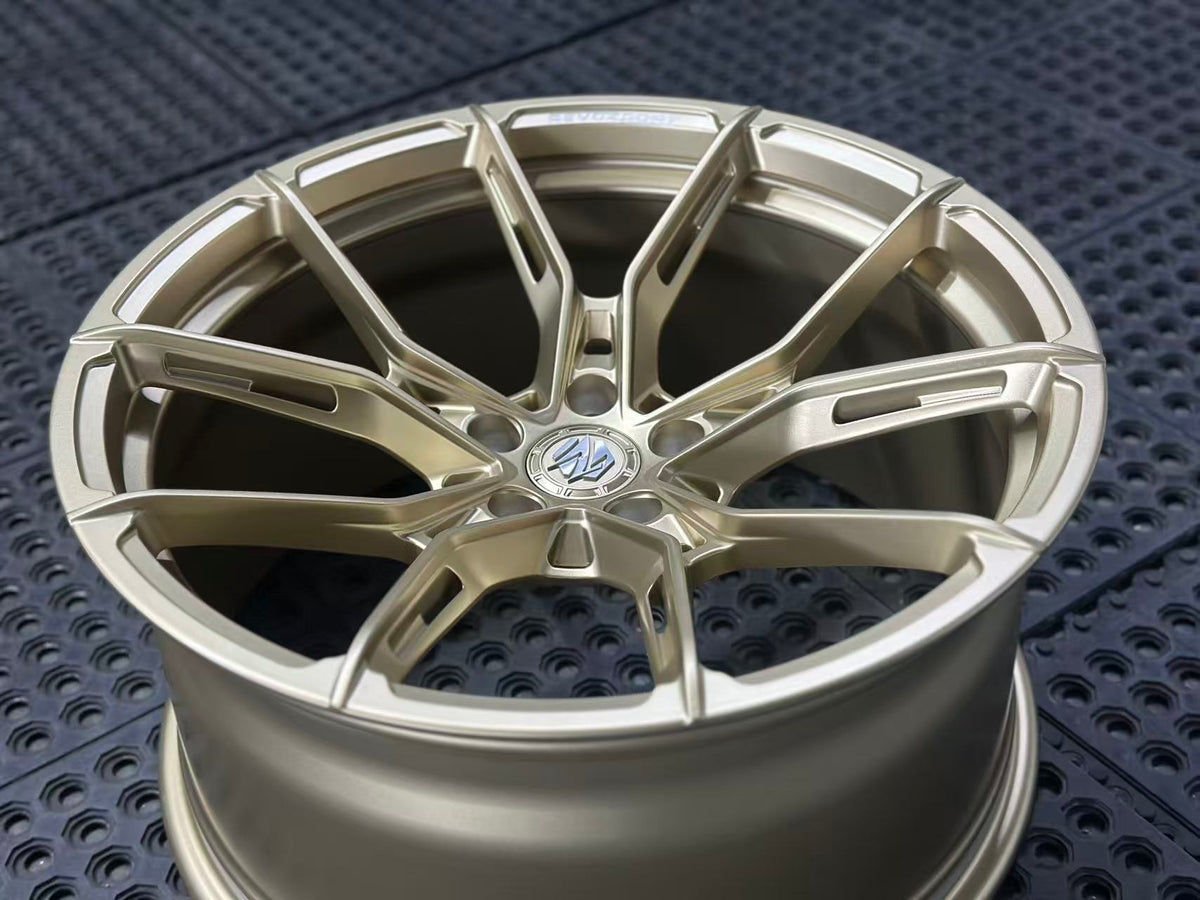 Bronze REVOZPORT forged alloy wheel with split multi-spoke design displayed on a black textured workshop floor.