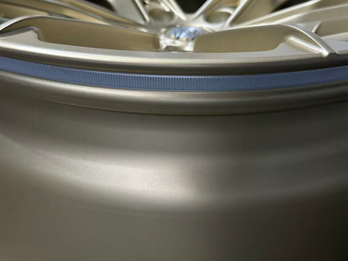 Bronze REVOZPORT forged alloy wheel with split multi-spoke design displayed on a black textured workshop floor.