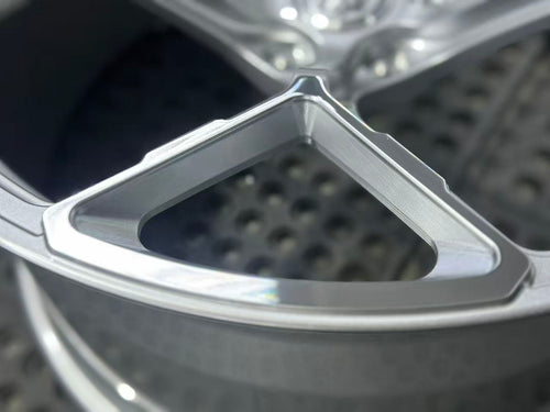 Silver forged alloy wheel with a multi-spoke design displayed against a black textured rubber floor.