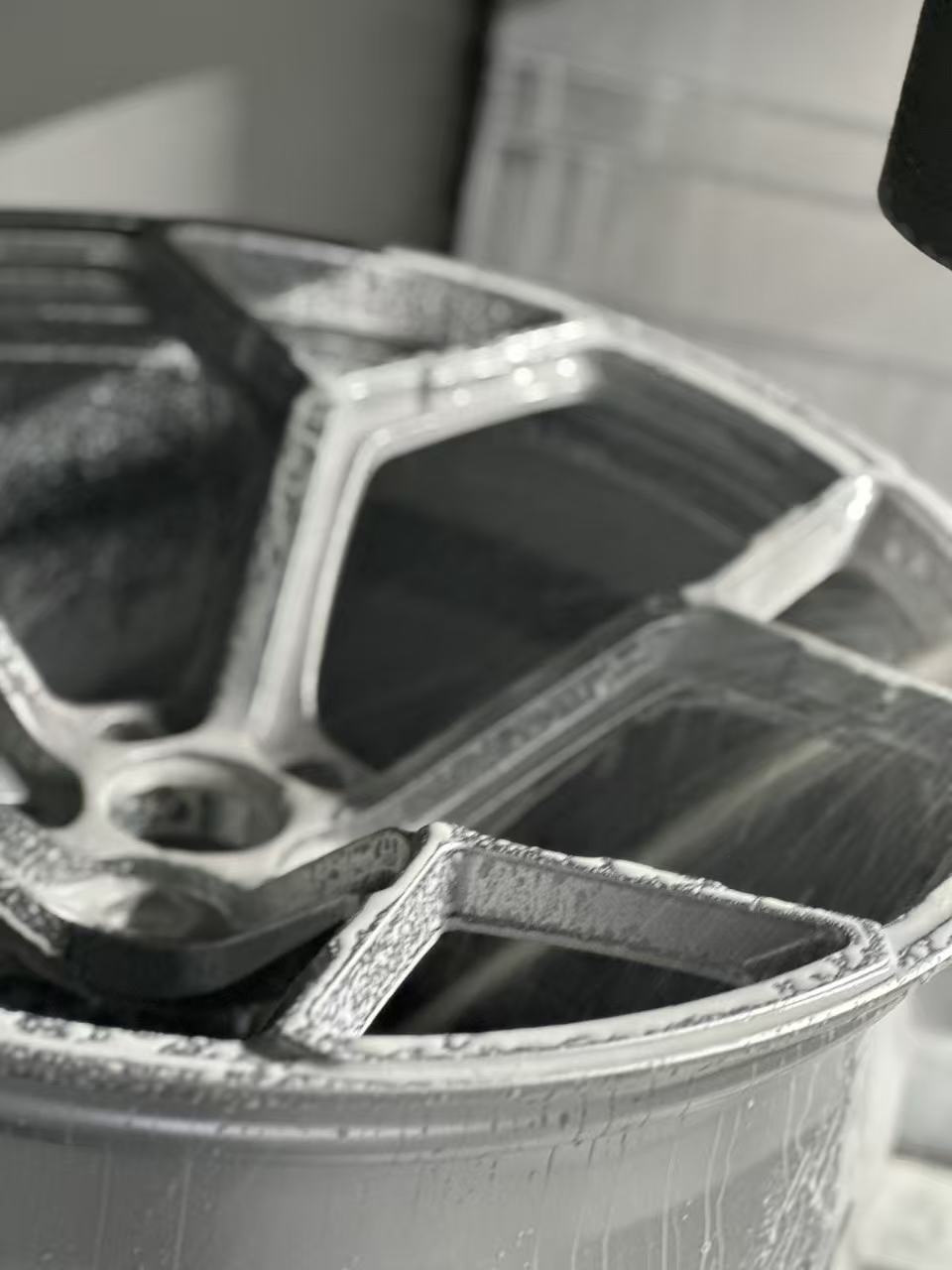 Silver forged alloy wheel with a multi-spoke design displayed against a black textured rubber floor.