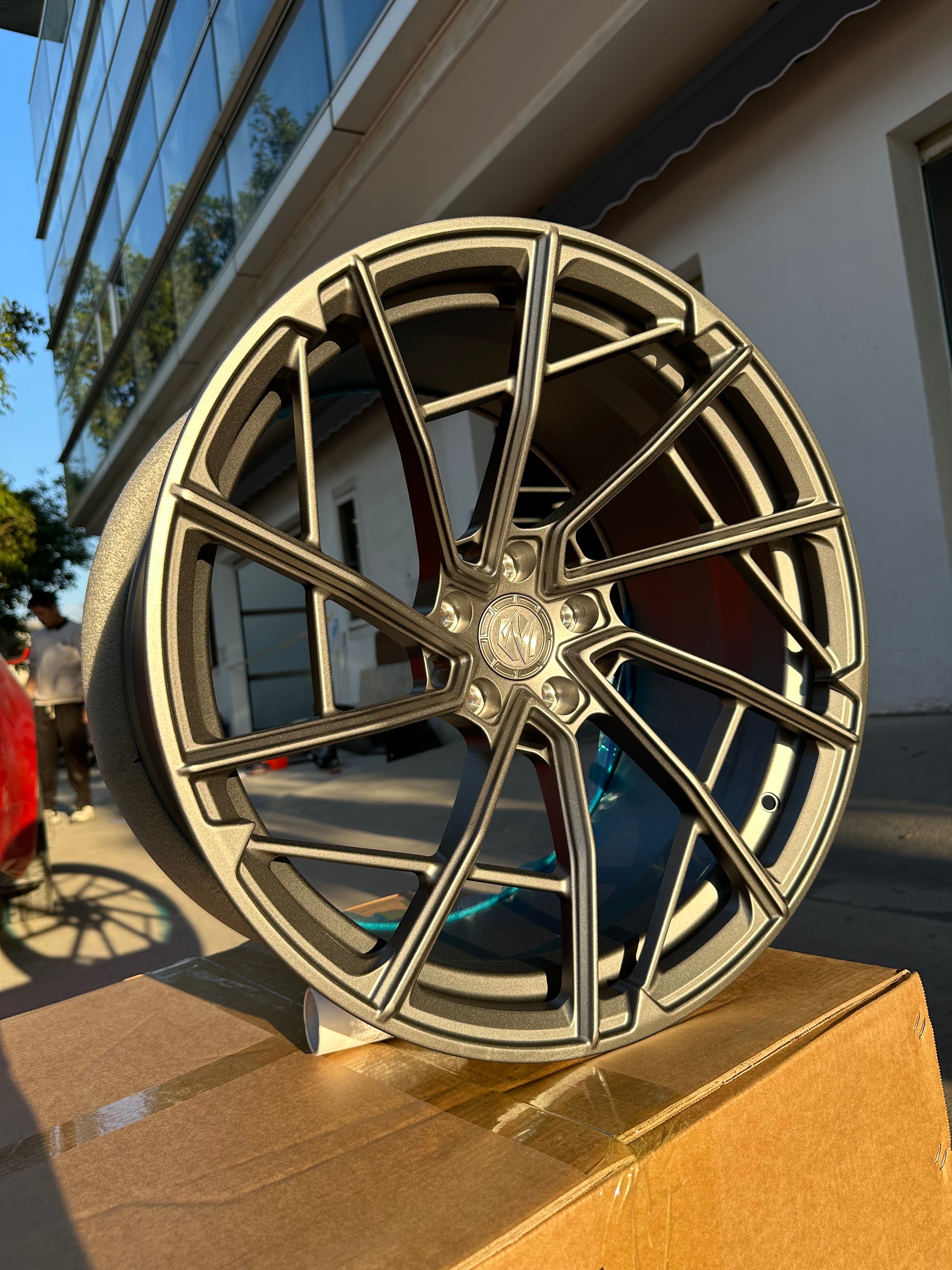 Matte gray REVOZPORT forged alloy wheel with an intricate split multi-spoke design displayed on a black textured workshop floor.