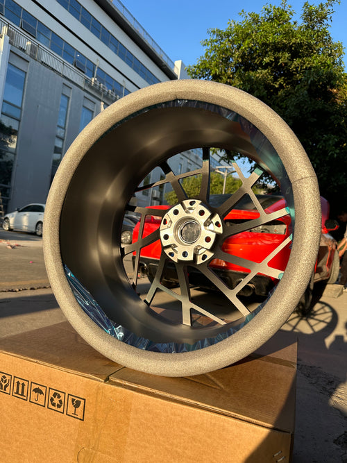 Matte gray REVOZPORT forged alloy wheel with an intricate split multi-spoke design displayed on a black textured workshop floor.