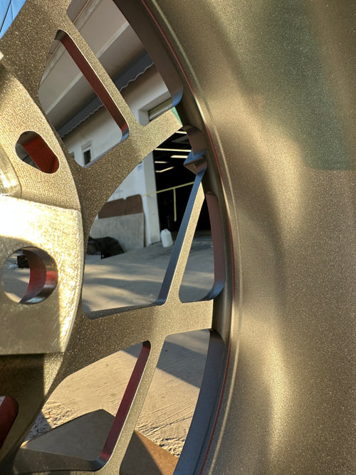 Matte gray REVOZPORT forged alloy wheel with an intricate split multi-spoke design displayed on a black textured workshop floor.