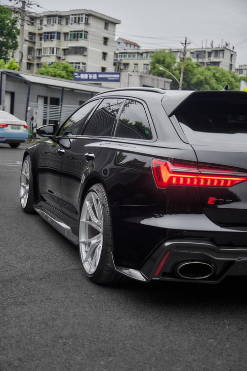 Black Audi RS6 Avant fitted with a REVOZPORT body kit and silver multi-spoke wheels, parked in an open lot surrounded by trees.