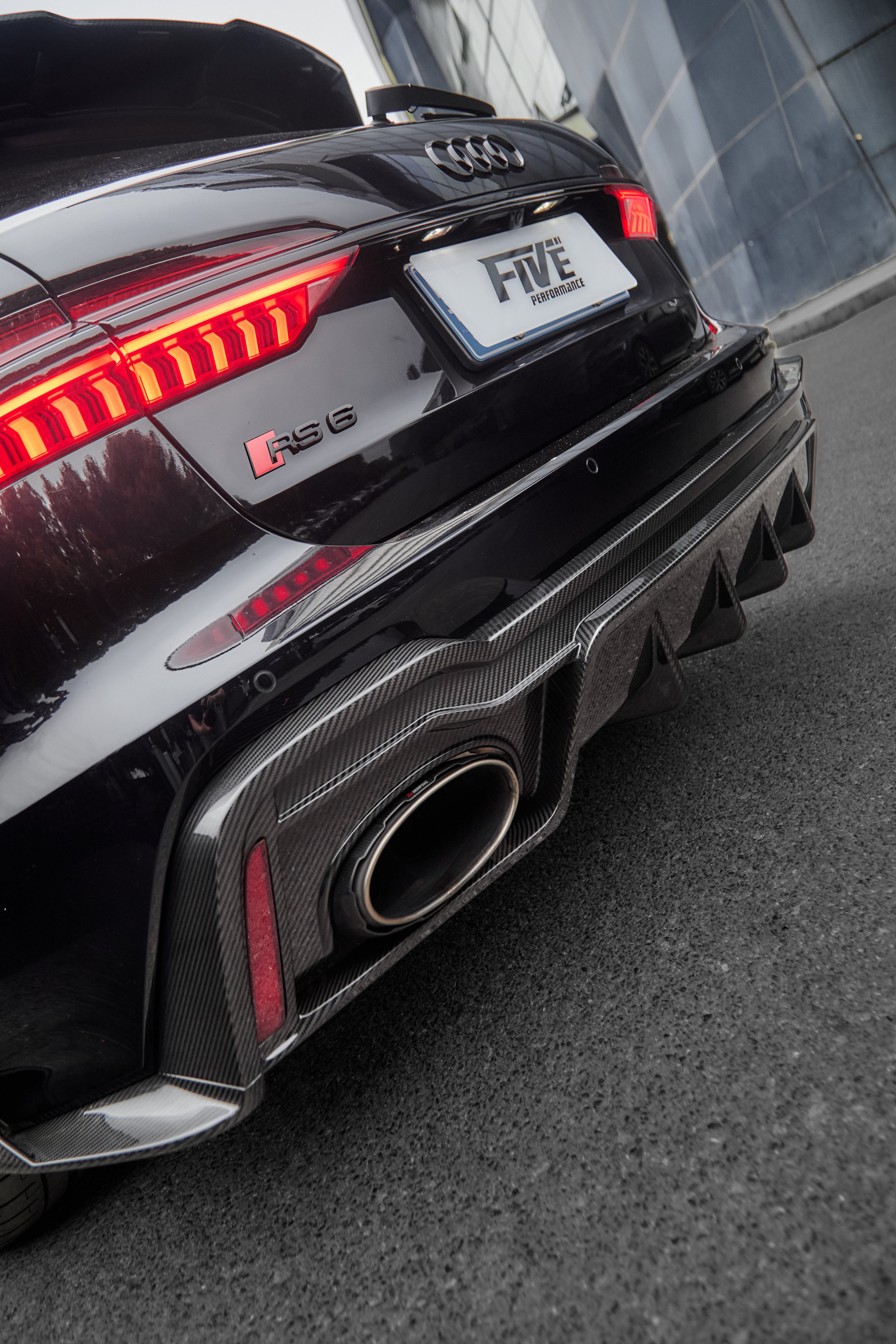 Black Audi RS6 Avant fitted with a REVOZPORT body kit and silver multi-spoke wheels, parked in an open lot surrounded by trees.