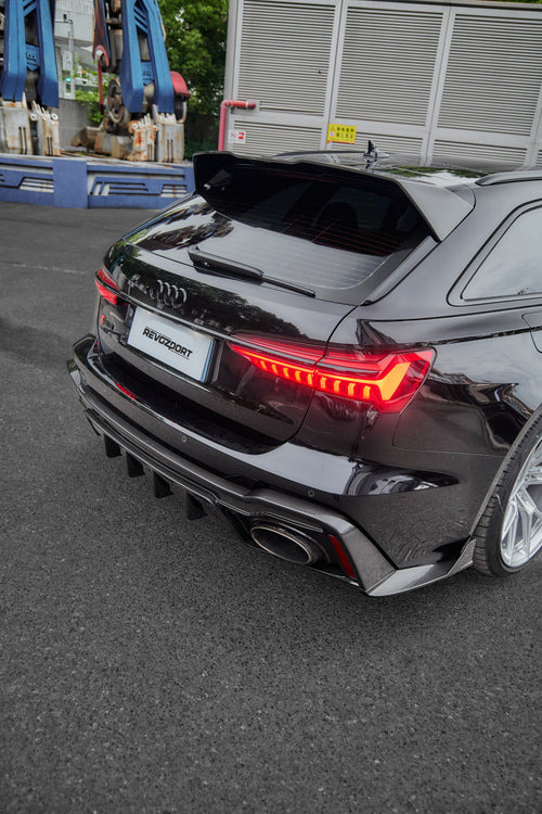 Black Audi RS6 Avant fitted with a REVOZPORT body kit and silver multi-spoke wheels, parked in an open lot surrounded by trees.