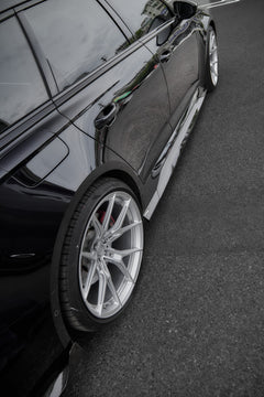 Black Audi RS6 Avant fitted with a REVOZPORT body kit and silver multi-spoke wheels, parked in an open lot surrounded by trees.