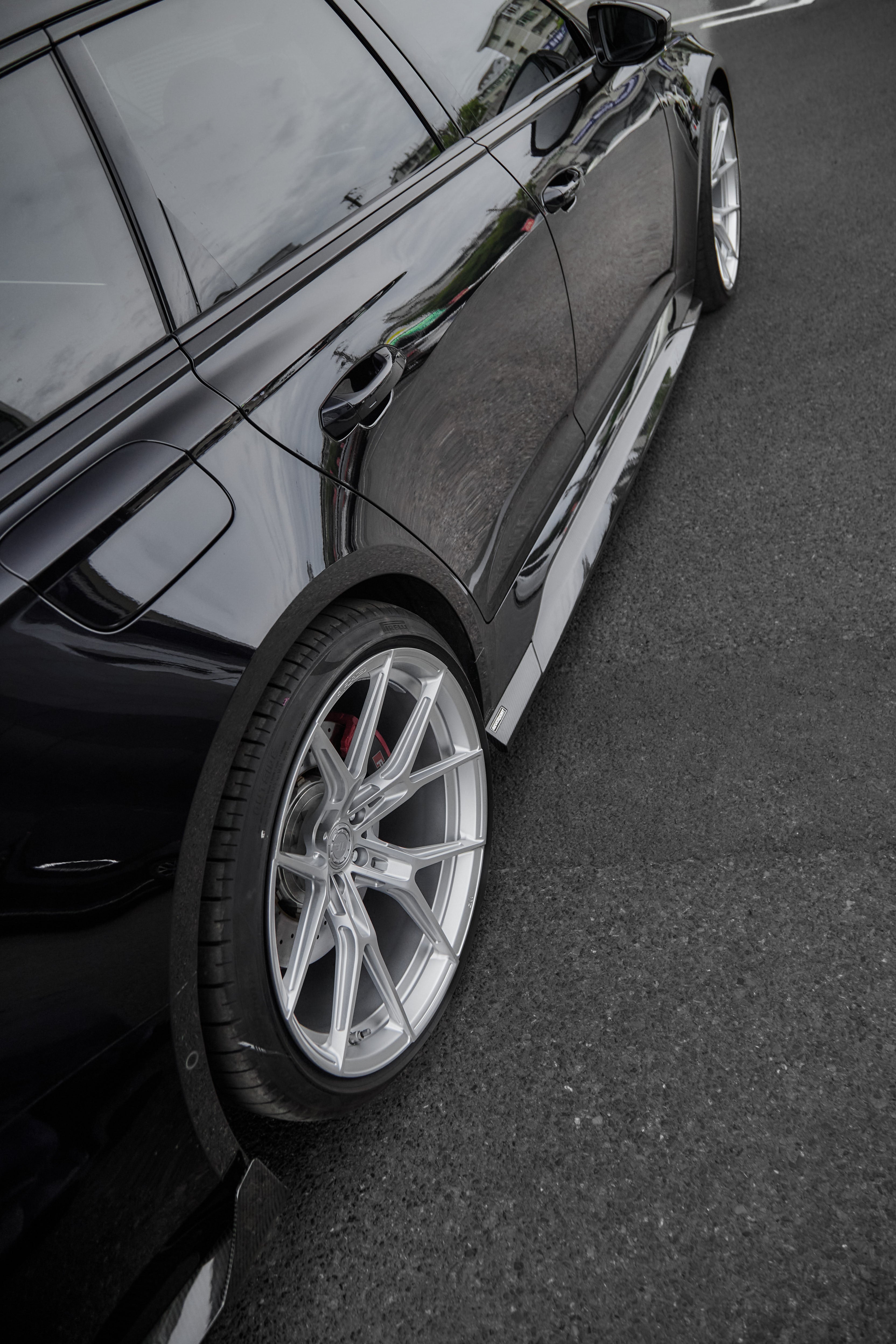 Black Audi RS6 Avant fitted with a REVOZPORT body kit and silver multi-spoke wheels, parked in an open lot surrounded by trees.