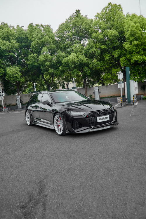 Black Audi RS6 Avant fitted with a REVOZPORT body kit and silver multi-spoke wheels, parked in an open lot surrounded by trees.
