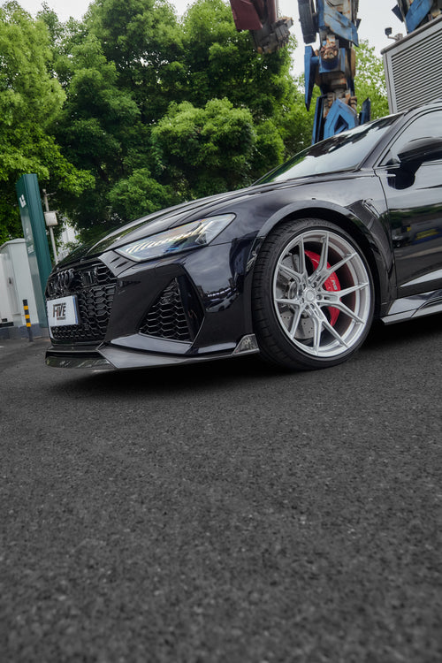 Black Audi RS6 Avant fitted with a REVOZPORT body kit and silver multi-spoke wheels, parked in an open lot surrounded by trees.