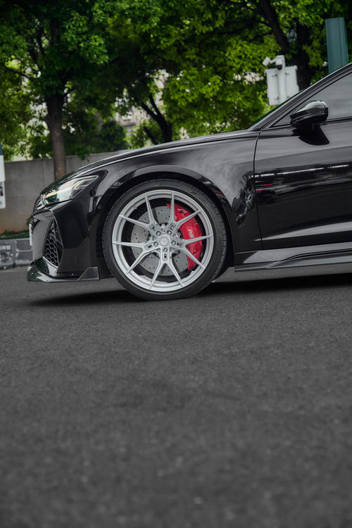 Black Audi RS6 Avant fitted with a REVOZPORT body kit and silver multi-spoke wheels, parked in an open lot surrounded by trees.