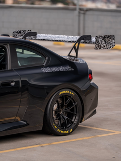 Gray BMW M2 featuring a REVOZPORT body kit with front lip, rear wing, canards, vented fenders, and hood, parked in an open rooftop lot.