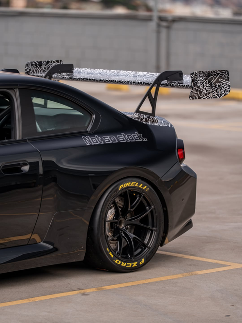 Gray BMW M2 featuring a REVOZPORT body kit with front lip, rear wing, canards, vented fenders, and hood, parked in an open rooftop lot.