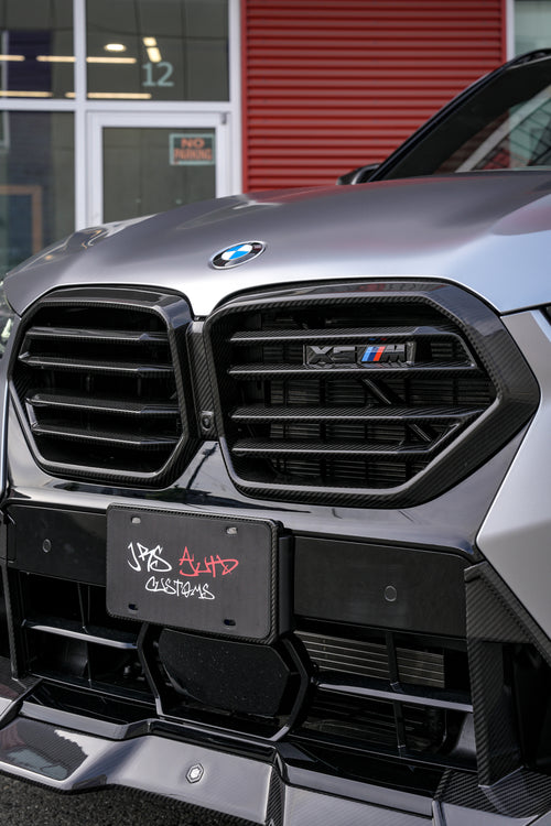 Gray BMW X5M featuring a REVOZPORT carbon fiber body kit with aggressive front lip, side skirts, and sporty aero styling parked outside a workshop.