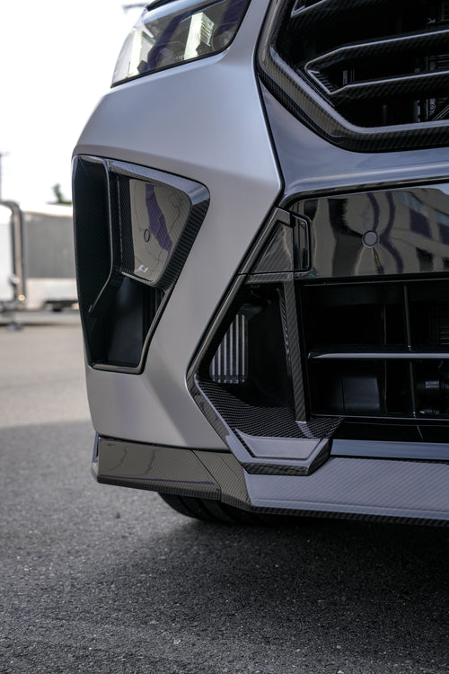 Gray BMW X5M featuring a REVOZPORT carbon fiber body kit with aggressive front lip, side skirts, and sporty aero styling parked outside a workshop.