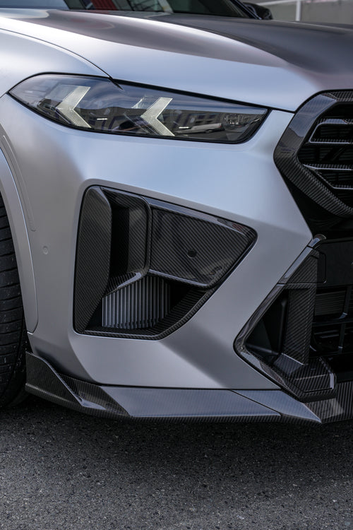 Gray BMW X5M featuring a REVOZPORT carbon fiber body kit with aggressive front lip, side skirts, and sporty aero styling parked outside a workshop.