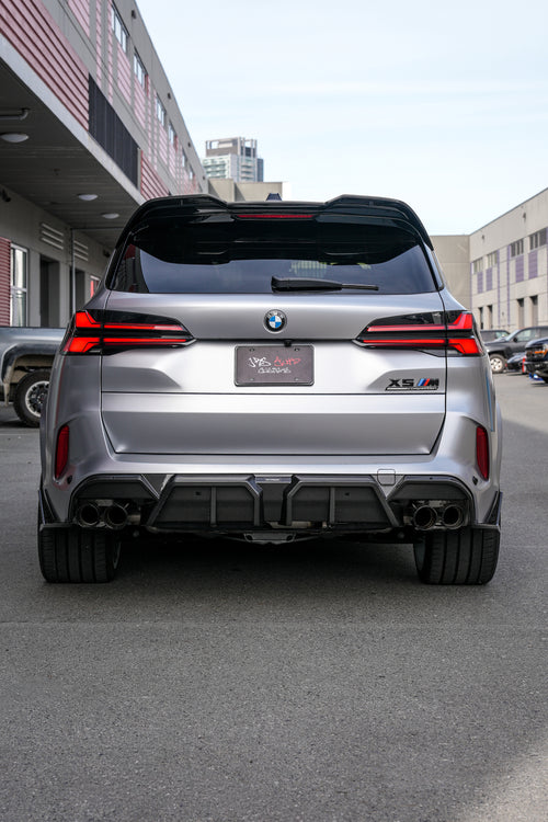 Gray BMW X5M featuring a REVOZPORT carbon fiber body kit with aggressive front lip, side skirts, and sporty aero styling parked outside a workshop.