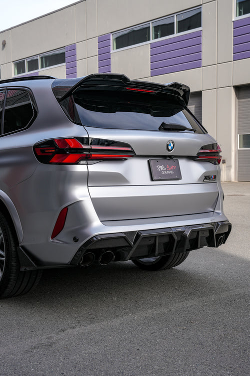 Gray BMW X5M featuring a REVOZPORT carbon fiber body kit with aggressive front lip, side skirts, and sporty aero styling parked outside a workshop.